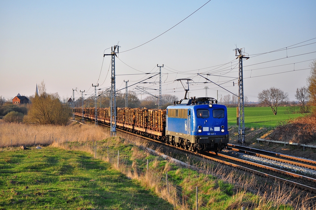 Mit einem Holzzug rollt die 140 037 der Press am 22.04.2013 durch Sildemow in Richtung Schwerin.