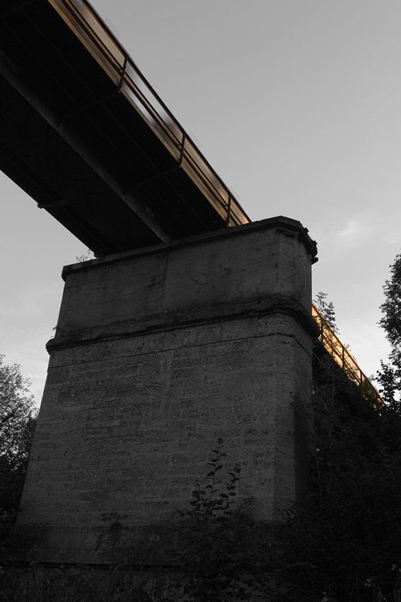 Mächtig wirkt die Eisenbahnbrücke, die den Bach  Schwillach  und eine Straße in Unterschwillach in ziemlich großer Höhe überquert. So wie es aussieht, wurde sie einst für einen zweigleisigen Ausbau der KBS 940 München - Mühldorf konstruiert.

Der Saaler Kalkzug aus Saal an der Donau nach München wies samt der BR 266.4 aus dieser Perspektive diesselbe Höhe auf, wie das Brückengeländer. Dazu ist auch die Farbe der Kalkkübel so grau, wie dessen mächtiger Pfeiler. So wurde hier ein  Colour-Key  angewendet.

Unterschwillach am 10.08.15