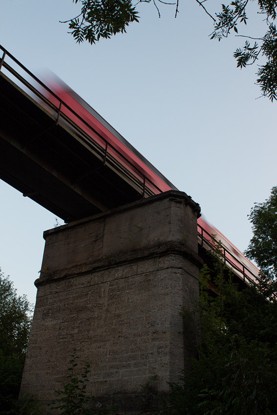 Mächtig wirkt die Eisenbahnbrücke, die den Bach  Schwillach  und eine Straße in Unterschwillach in ziemlich großer Höhe überquert. So wie es aussieht, wurde sie einst für einen zweigleisigen Ausbau der KBS 940 München - Mühldorf konstruiert.

Eine 218 überquerte sie am Abend des 11.08.15 mit einem kurzen Bn-Wagenzug in Richtung Mühldorf.