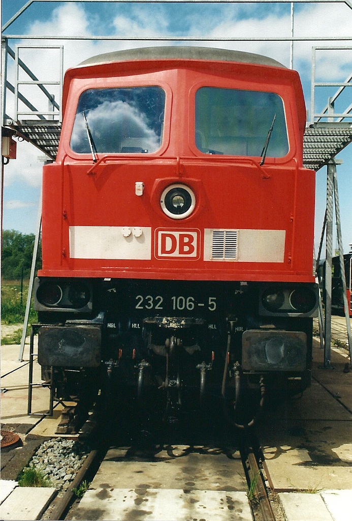 Am 20.05.2004 steht die 232 106 in Rostock-Seehafen.Im verkehrsroten Lack zeigt sie sich mit UIC-Dose,verschlossenen Buchsen der Doppeltraktionssteuerung,metallgefassten Frontscheiben sowie den geteilten Griffstangen.