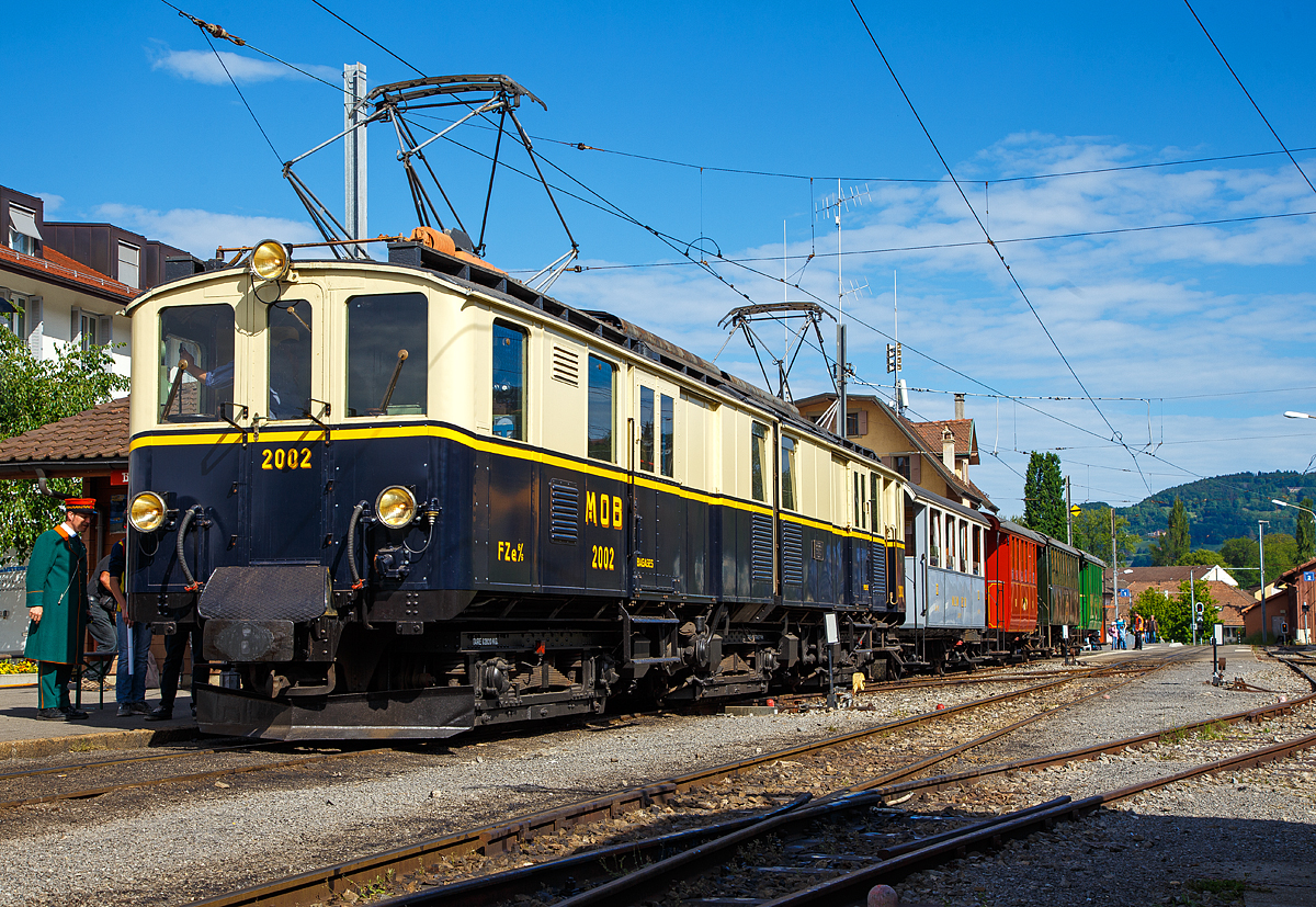 50 Jahre BC - MEGA STEAM FESTIVAL der Museumsbahn Blonay–Chamby:
Bevor wir nach Vevey herunter „surften“...
Konnten wir noch im tollen Morgenlicht den wundersch�ne Gelenktriebwagen ex MOB DZe 6/6 2002, bzw. FZe 6/6 2002 bestaunen und fotografieren. Hier steht er am 21.05.2018 im Bahnhof Blonay mit einem Zug zur Abfahrt zum Museum bereit.

Der Triebwagen Gep�ck- und Postabteil wurde 1932 von SIG unter der Fabriknummer 3703 gebaut, der Elektrische Teil ist von BBC. Der Gep�cktriebwagen war bis 1996 im Einsatz und wurde dann in der Remise Gstaad Abgestellt und gammelte vor sich hin, bis er im Juli 2008 zur Museumsbahn Blonay–Chamby ging.

Die MOB (Montreux–Berner Oberland-Bahn) beschaffte f�r die Bespannung des “Golden Mountain Pullman Express” die beiden zweiteiligen Gelenktriebwagen FZe 6/6 2001 und 2002 (MOB-intern immer „Lokomotiven“ bzw. „Gep�cklokomotiven“ genannt). Nachdem der Expresszug schnell wieder eingestellt wurde (vor der Lieferung), fanden die beiden Gelenktriebwagen ein neues Bet�tigungsfeld im schweren Schnellzug- und G�terzugverkehr bzw. bespannten Sonderz�ge mit den bei der MOB verbliebenen Salonwagen.

Riesig sind sie, mit ihren immerhin 17 m L�nge, sind diese Gelenktriebwagen eine eindrucksvolle Erscheinung. Bis zur Einf�hrung der Baureihe GDe 4/4 6000, also rund f�nfzig Jahre lang, waren sie au�erdem mit ihren rund 1.000 PS die leistungsst�rksten Gleichstrom-Lokomotiven der Schweiz. 

Es war auch wie hier im Bild �blich das beide Stromabnehmer angehoben sind, da wegen der relativ geringen Spannung sehr hohe Stromst�rken erforderlich sind.

Die urspr�ngliche Bezeichnung war „FZe 6/6“ (Triebwagen mit Gep�ck- (F) und Postabteil (Z)) wurde sp�ter in „DZe 6/6“ ge�ndert. Eine solche Umzeichnung fand europaweit irgendwann nach dem 1. Januar 1962 statt, sie entsprach dem RIC-Reglement (Regolamento Internazionale Carrozze, ein �bereinkommen �ber die gegenseitige Benutzung der Personen- und Gep�ckwagen im internationalen Verkehr). 

Die beiden Fahrzeuge 2001 und 2002, trugen nie irgendwelche Wappen oder Namen, sie behielten allerdings bis heute die Pullman-Lackierung in dunkelblau/cr�me mit gelbem Seitenstreifen

TECHNISCHE DATEN:
Fahrzeugbezeichnung: DZe 6/6 bzw. (FZe 6/6)
Anzahl Fahrzeuge: 2  (2001 und 2002)
Inbetriebsetzung: 1932
Spurweite: 1.000 mm
Achsanordnung: Bo'Bo'Bo' 
Dienstgewicht: 62,8 t
L�nge �ber Kupplung: 17.000 mm
Kastenl�nge: 2 x 7.850 mm
Fahrzeugh�he: 3.550 mm
Fahrzeugbreite: 2.700 mm
Drehgestellabstand: 2 x 5.500 mm
Achsabstand im Drehgestell: 2.300 mm
Treibraddurchmesser (neu): 945 mm
H�chstgeschwindigkeit: 55 km/h
Maximale Leistung am Rad 	6 x 132 kW = 738 kW	
Getriebe�bersetzung: 1:6.94
Ladefl�che Gep�ck- / Postraum: 10 m� / 8 m�	 (4t)
Stromsystem: 900 V DC
