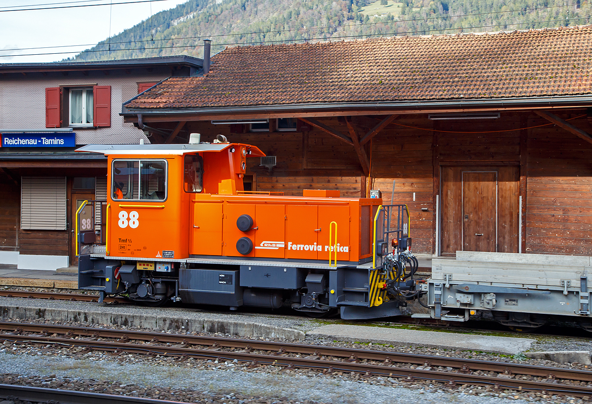 Äußerlich sieht er noch so aus wie der Alte, aber innerlich ist er komplett neu....
Der aus dem Refitrprogramm gekommene RhB Tmf 2/2 88 ist am 01.11.2019 im Bahnhof Reichenau-Tamins abgestellt, aufgenommen aus einem RhB Zug heraus.

Die Tmf 2/2  wurde 1992 von RACO (Robert Aebi AG, Regensdorf, Schweiz) unter der Fabriknummer 1989 gebaut und an die RhB geliefert. Die RACO Typenbezeichnung ist 420 CT 4H.Die Tmf 2/2 sind die mit Funkfernsteuerung ausgerüsteten Traktoren mit Verbrennungsmotoren der Rhätischen Bahn (RhB). Zwischen 1991 und 1994 wurden von RACO sechs dieser Tmf 2/2 mit den Nummern 85 bis 90 beschafft. Der Tmf 2/2 88 wurde nach dem Umbau in der RhB Werkstatt in Landquart Anfang Oktober 2018 erfolgreich durch das BAV abgenommen und durfte einige Tage später den Betrieb aufnehmen.

Die RhB Tmf 2/2 88 ist der Prototypenumbau, die im Rahmen des Projekts «Refit Baudienstfahrzeuge Tm(f) 2/2» werden die sechs Rangiertraktoren Tmf 2/2 85-90 mit den Baujahren1990 bis 1994, nach und nach, durch diverse Umbau- und Erneuerungsarbeiten fit für die Zukunft gemacht. Zu immer höheren Unterhalts- und Revisionskosten führen nach den Jahren im Betrieb einige Komponenten aus dem Antriebsstrang und dabei vor allem der Cummins-Dieselmotor. Aufgrund seines Alters kann dieser Motorentyp nicht mehr als Neuteil beschafft, sondern nur noch revidiert werden.

Aus diesem Grund hat sich die RhB vor einigen Jahren entschieden, diesen Dieselmotor bei den Tmf 2/2 85-90 zu ersetzen. Nach umfangreichen Untersuchungen wurde bald klar, dass nebst dem Dieselmotor auch einige andere zentrale Fahrzeugkomponenten von Obsoleszenz betroffen sind und weitestgehend nicht mehr den heutigen technischen Ansprüchen genügen. Dazu gehören Getriebe, Partikelfilteranlage, Kühlungsanlage, Hydraulik, Pneumatik, Bremsmechanik wie aber auch die komplette elektrische Einrichtung, die Fahrzeugsteuerung, die Sicherheitseinrichtung und die Fahrdatenvisualisierung. Grob umschrieben in etwa alles außer dem Chassis, Kabine und Achsen.

Antriebsstrang:
Aufgrund der betrieblichen Anforderungen entschied die RhB, den Reihen 6-Zylinder durch einen V8-Dieselmotor von Deutz zu ersetzen. Der neue Motor ist dank seiner V-Bauweise sehr kompakt und kann je nach Drehzahl bis zu 30 % mehr Leistung abgeben als der bestehende. Um diese Leistung optimal auf die Schienen zu bringen, wurde das bestehende Lastschaltgetriebe durch ein automatisches Wendegetriebe der Firma Voith ersetzt. Dieses Getriebe sowie auch die komplette Kühlanlage wurden von Voith auf die Leistungsdaten des Motors optimal abgestimmt. Ein großer Benefit nebst der Leistungssteigerung und der „Einfachheit“  des Antriebsstranges liegt darin, dass die Gangschaltung – mit welcher die restlichen Tmf  2/2 gestraft sind – nicht mehr von Relevanz ist. Dank dem neuen Automatikgetriebe lässt sich die Geschwindigkeit stufenlos und ohne Leistungseinbruch zwischen V null und V max einstellen.

Fahrzeugsteuerung und Fahrdatenvisualisierung
Die bestehende KraussMaffei-Fahrzeugsteuerung wurde durch eine von Selectron, die RhB-Standard ist, ersetzt. Die Antriebsstrangkomponenten (Dieselmotor / Getriebe) wie auch Fahrzeugkomponenten wie beispielsweise Display, Funkfernsteuerung usw. kommunizieren über einen Fahrzeugbus mit der Fahrzeugsteuerung. Dadurch erleichtert sich die Fehlerdiagnose und es konnten viele elektromechanische Komponenten eingespart werden. Die Fahrzeugdaten werden dem Lokführer über Displays visualisiert.

TECHNISCHE DATEN der RhB Tmf 2/2 88 (Refit):
Baujahre: 1991/92 und 1994
Spurweite: 1.000 mm (Meterspur)
Achsfolge: B
Länge über Puffer:  7.490 mm
Achsabstand: 3.750 mm
Breite: 2 700 mm
Eigengewicht:  24 t
Höchstgeschwindigkeit: 60 km/h (60 km/h Schleppfahrt)
Treibraddurchmesser: 	750 mm
Motorentyp: Deutz V8-Dieselmotor 
Weitere Daten wie auch Motor- und Getriebetyp sind mir leider noch unbekannt.
