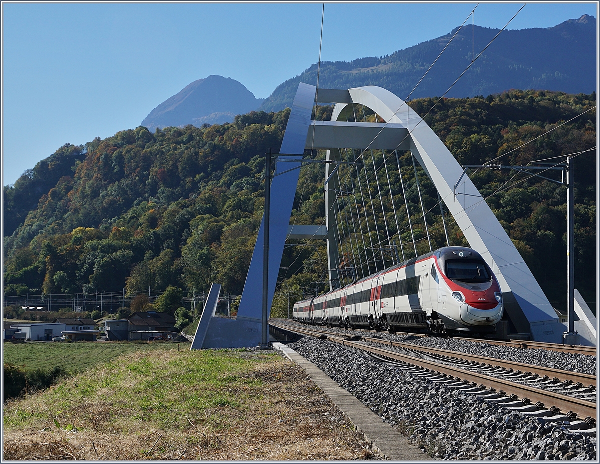 Fast 23 Meter über die Gleise wölben sich die beiden Bögen der SBB Brücke  Massongex , die zwischen Bex und St-Maurice über die Rhone führt. Die Brücke weist eine Spannweite von 125.8 Meter auf und gilt als längste Stählerne Eisenbahnbrücke der Schweiz. Sie ersetzt seit 2016 die beiden aus den Jahren 1903 und 1924 stammenden eingeleisigen Stahlbrücken. (Tech. Ang. Quelle: TEC21 Nr 41). Das Bild zeigt einen SBB ETR 610 der Als EC 32 von Milano nach Genève unterwegs ist. 11. Okt. 2017