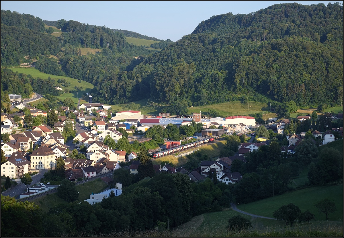 Umleiterverkehr auf dem L�ufelfingerli. Ein IC hat in L�ufelfingen gerade den Hauensteintunnel verlassen, rechts kann man gerade noch den Tunneleingang erkennen. Da die alte Bergstrecke namensgleich mit der Basislinie ist, wurde die Gemeinde L�ufelfingen im Bild der neue Namensgeber, obwohl die Strecke eigentlich als zweit�lteste Bahnlinie der Schweiz ist den Vorrang haben sollte... ;-) Im Hintergrund ist deutlich der Mittelgebirgscharakter des Jura zu erkennen, der den Bau der Strecke erschwerte. So dauerte es 4 Jahre vom ersten Zug 1854 bis zur vollst�ndigen Er�ffnung, leider wurden bei einem Brand w�hrend des Tunnelbaus 63 Menschen durch Kohlenmonoxid vergiftet. Juli 2018.