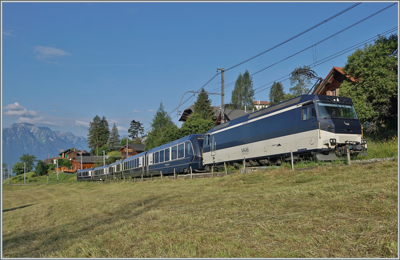 Des öfteren habe ich bereits angedeutet, dass  meine  gern genutzten MOB Fotostellen in der näheren Umgebung sich infolge Gegenlicht kaum für den GoldenPass Express eignen. Nun habe ich eine Ausnahme gefunden: Bei Les Avants im Hochsommer ist der erste Zug perfekt im Licht und zudem in seiner ganzen, nun normalen Länge zu sehen: Die MOB Ge 4/4 8002 ist mit dem Golden Pass Express GEX 4064 von Montreux nach Interlaken Ost kurz vor Les Avants unterwegs. In Zweisimmen wird eine BLS Re 465 die MOB Ge 4/4 8002 ablösen. Im Hintergrund die Walliser- und Savoyer Alpen und weit unten der Lac Léman.
Zum Schluss die Bildvariante mit dem Bildfüllenden GPX. 

 28. Juni 2024 