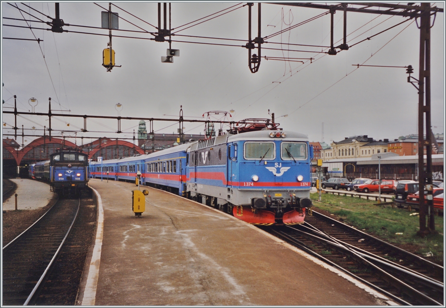Die SJ Rc6 1374 verlässt mit einem Reisezug Malmö C, während im Hintergrund sich die SJ Ue 998 um den angekommenen D 318  Nils Holgersson  von Berlin kümmert.

Analogbild vom 30. April 1999