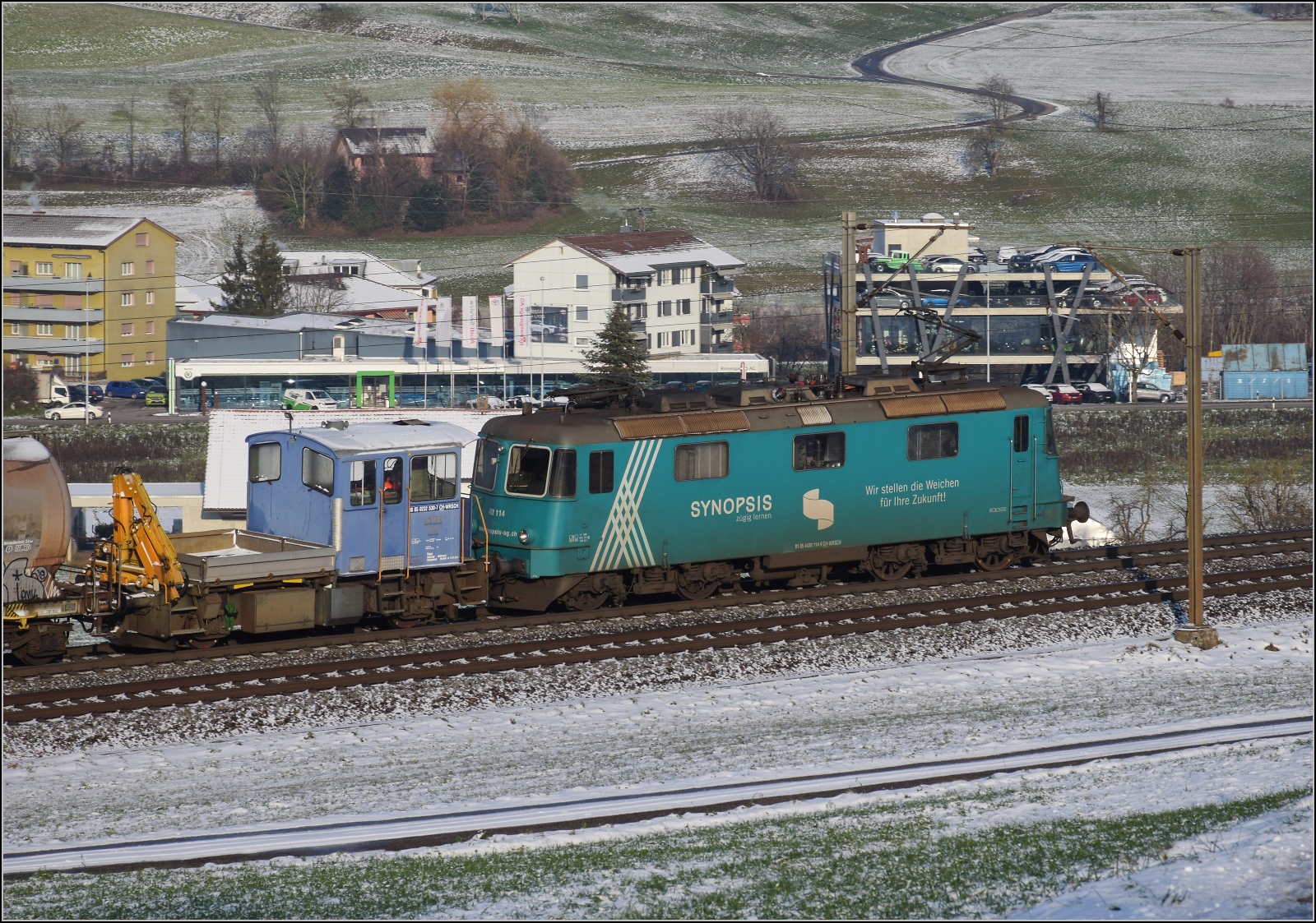 Re 430 114 von WRS mit Synopsis-Werbung schleppt die Rangierhilfe Tm III 9530 mit über den Bözberg. Frick, Dezember 2022.

