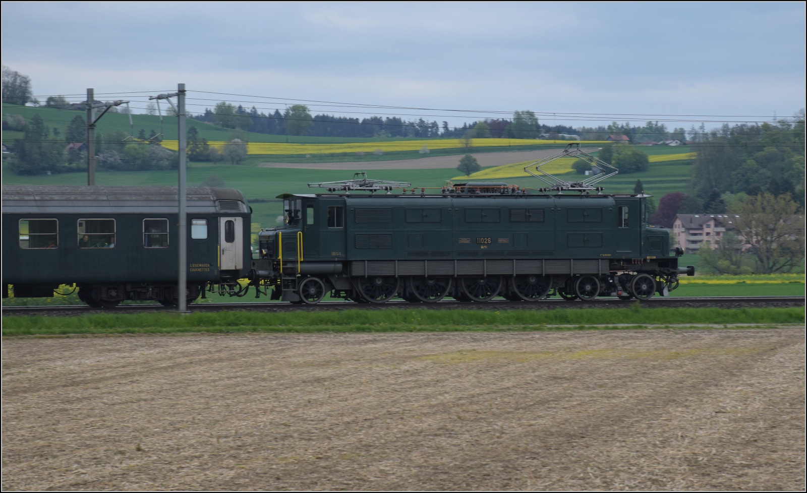 Rundfahrt vom Bodensee durchs Emmental mit 23 058 und Ae 4/7 11022.

Hier schiebt Ae 4/7 11026 den Zug, während sich die Dampflok offenbar bei Schmierdampf ausruht. Hendschiken, April 2023. 